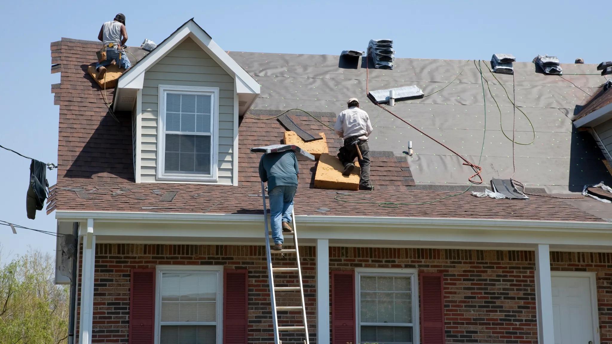 A group of construction workers on a residential roof replacing shingles.