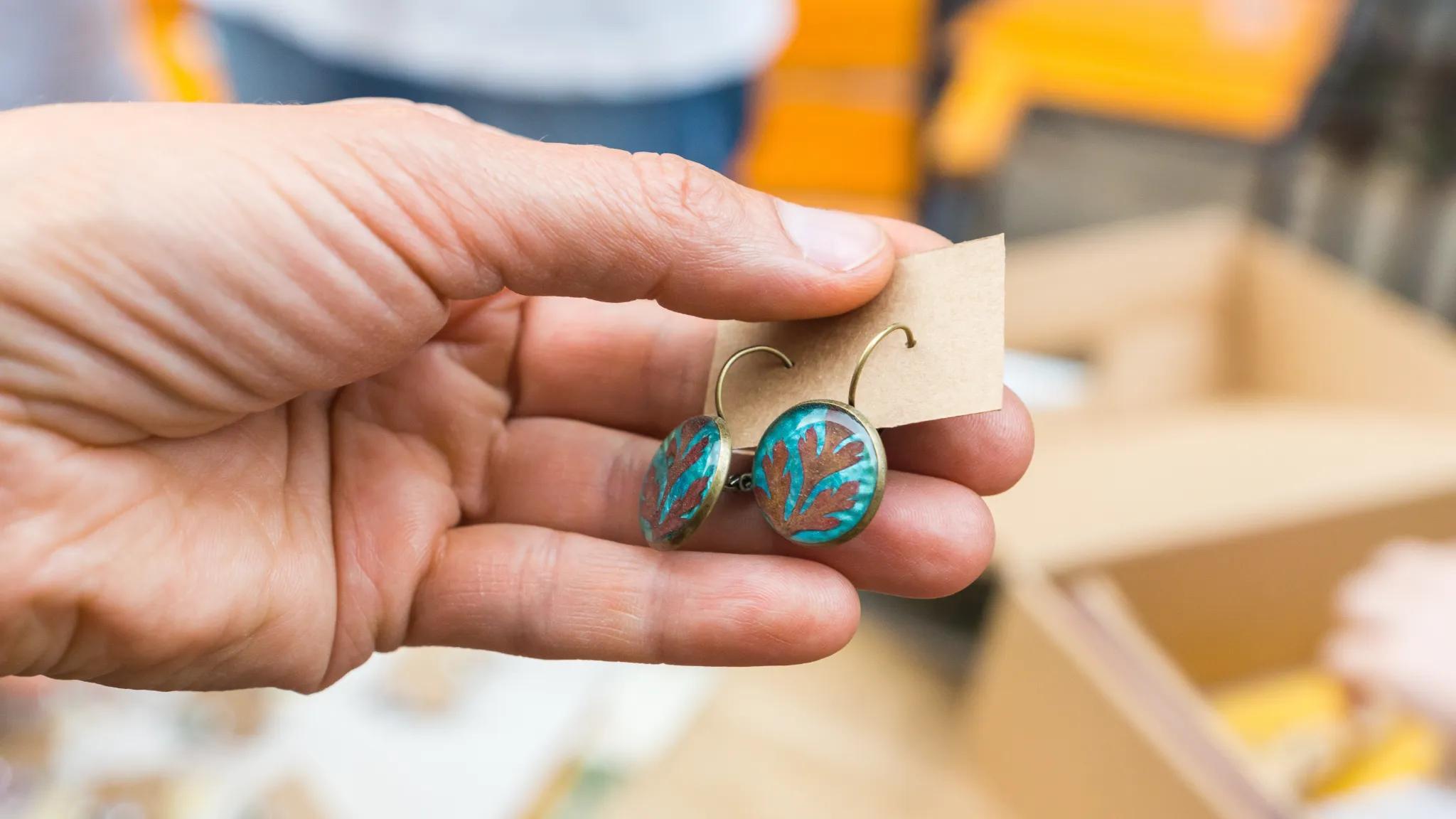 Person holding a pair of turquoise-colored earrings.