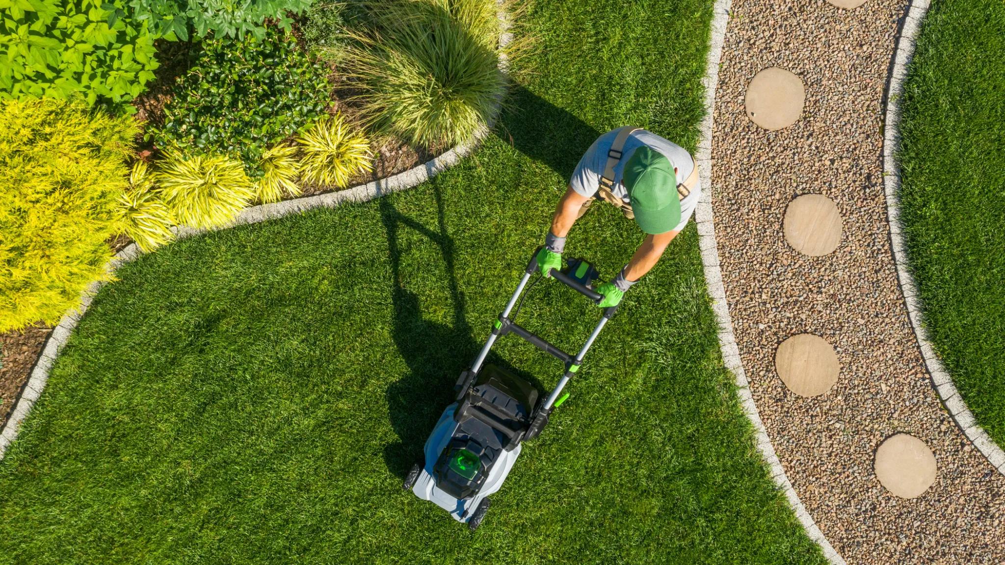 Landscaper pushing a lawn mower through grass.