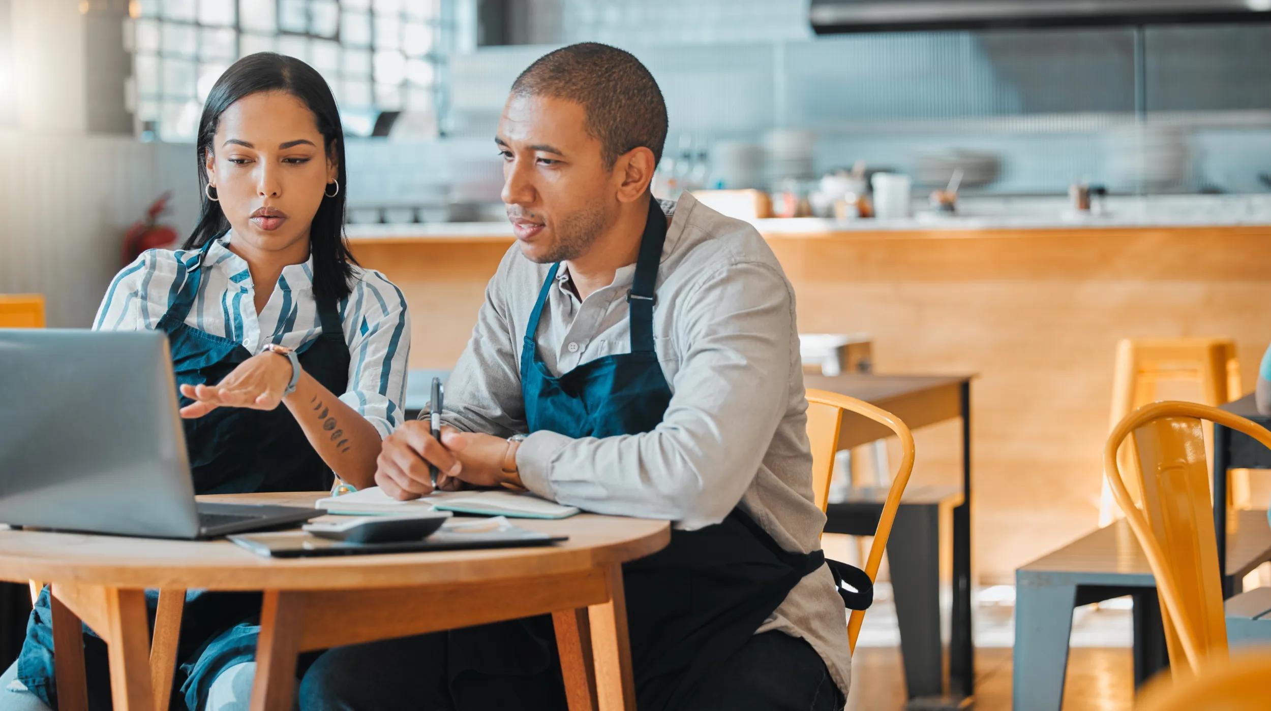 a man and a woman sitting at a table looking at a laptop