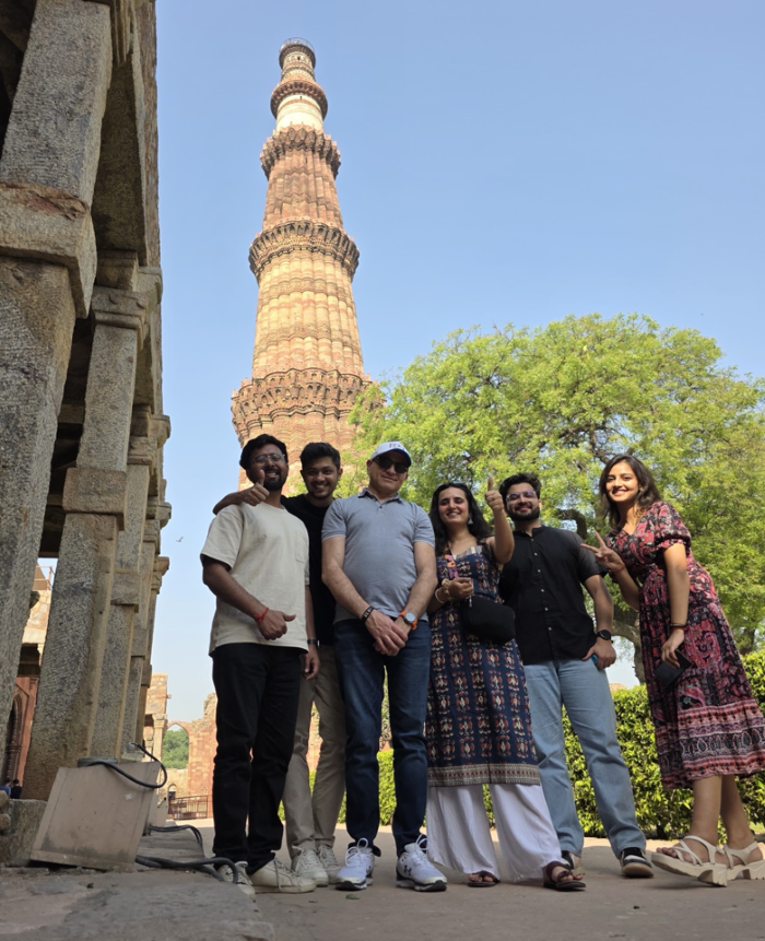 a group of people posing for a photo in front of a tall tower with Qutub Minar in the background