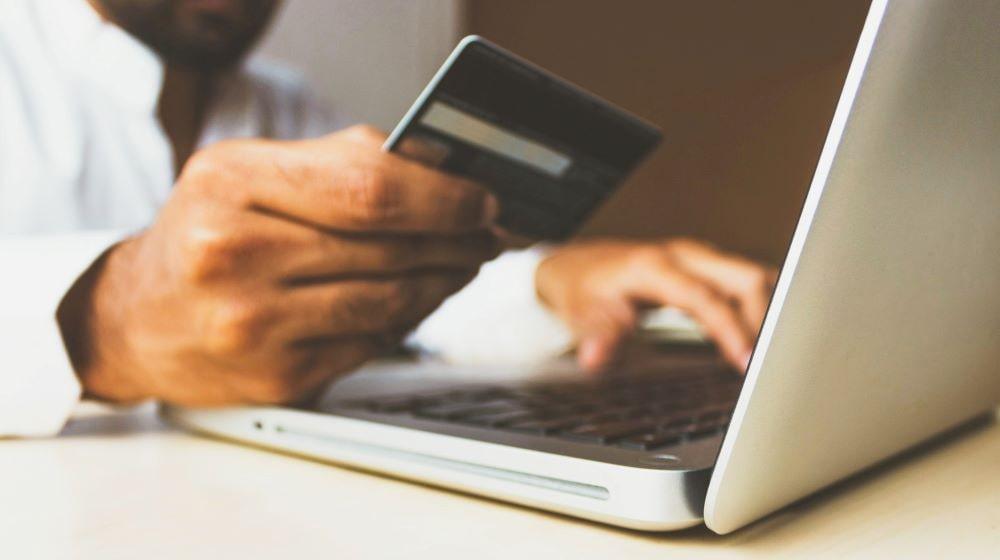 Person Holding Credit Card Over Laptop