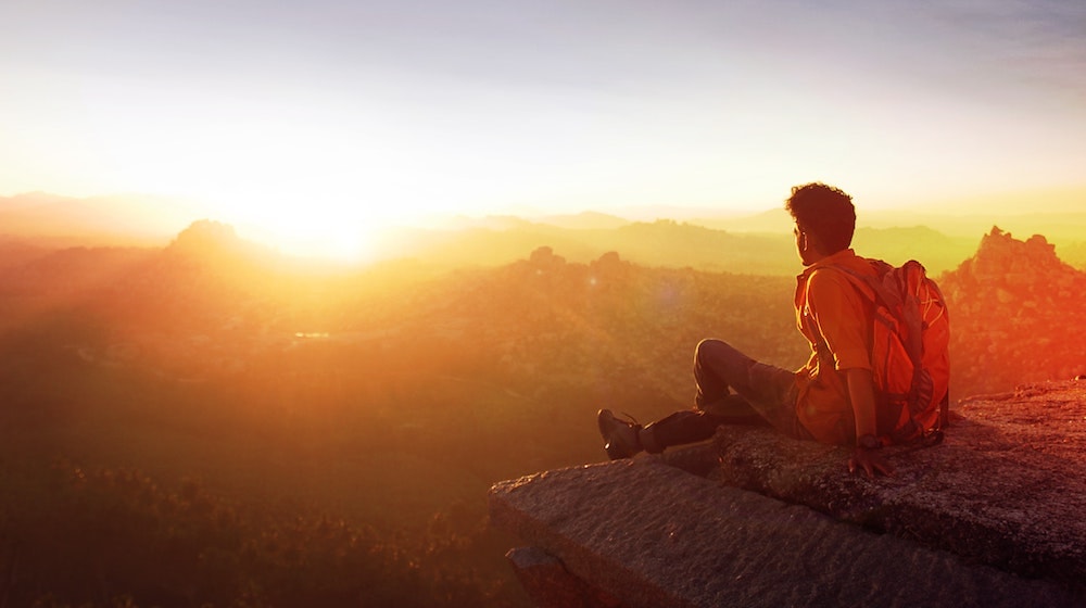Man Sitting on Edge of Mountain at Sunset