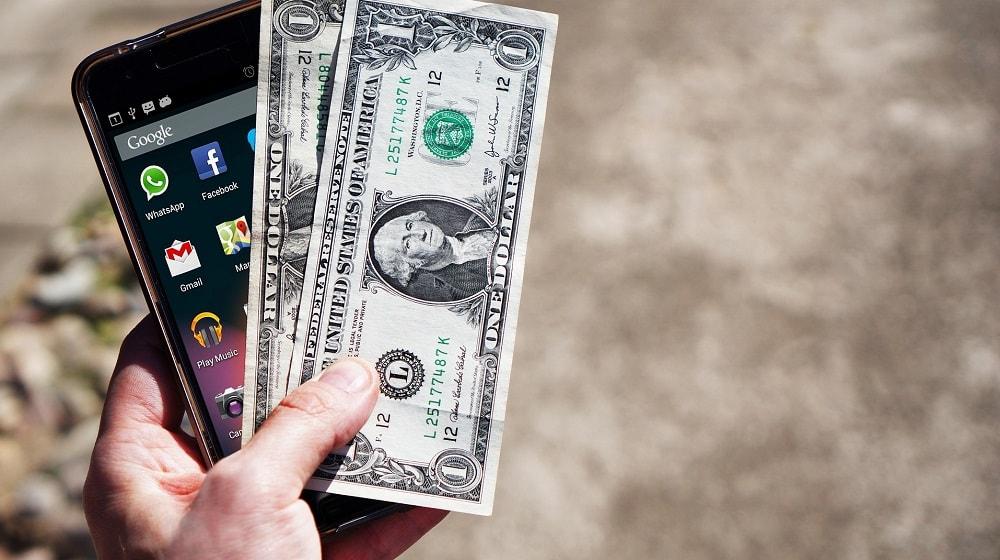 Hand Holding Mobile Phone And Cash Illustrates How to Sell Your Domain Name