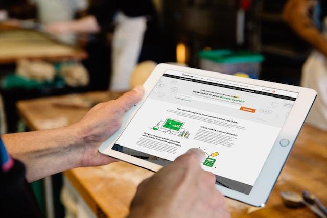 Hands Holding iPad Scrolling Through GoDaddy Domain Valuation Tool Website Page