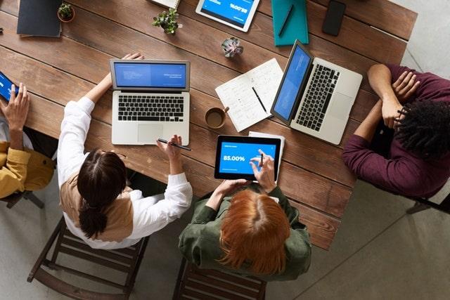 Team Meeting With Laptops And Tablets On A Large Desk