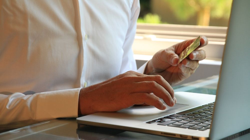 Man Holding Credit Card at Laptop Represents Online Sales Tax