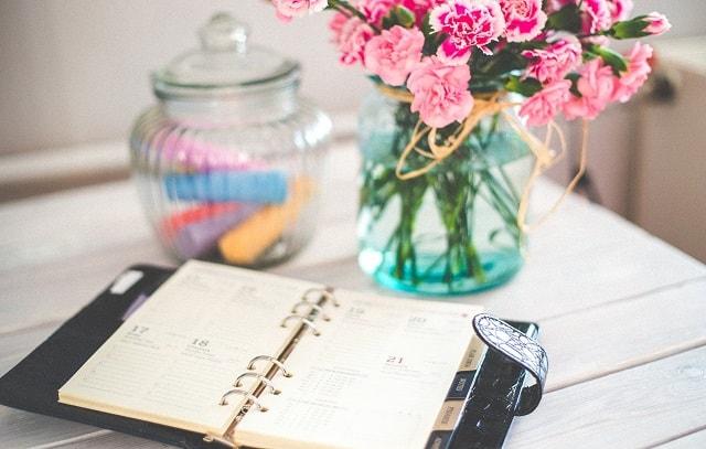 Open Planner On A Desk Near Vase Of Flowers