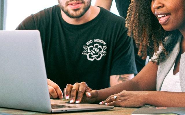 Two People Work Side by Side on a Laptop